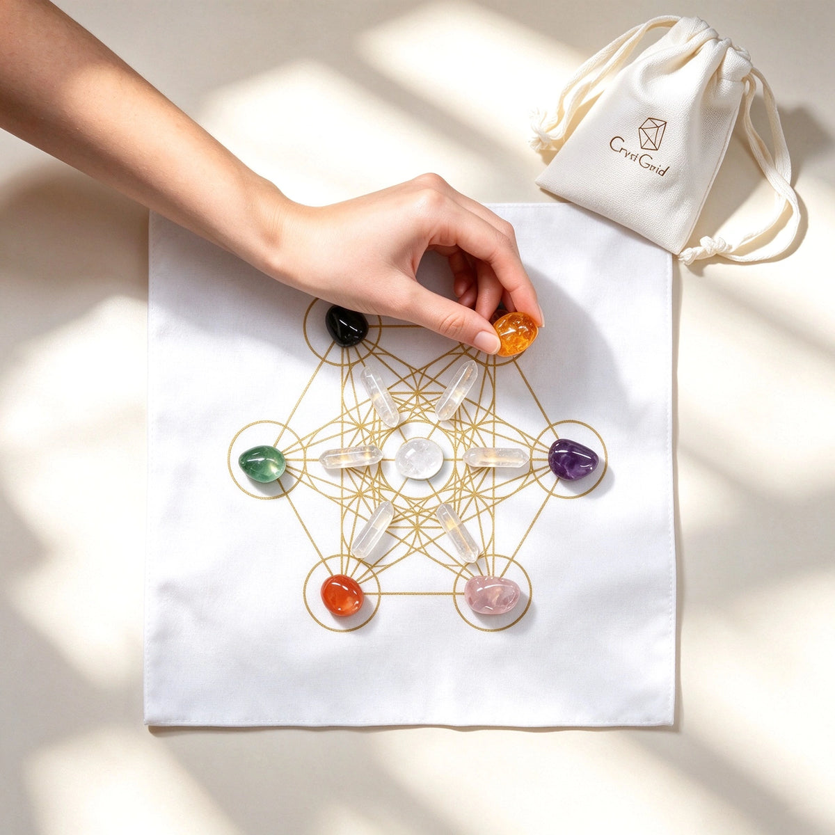 Hand placing an amber chakra stone on the gold Metatron grid cloth, CrystGrid pouch in the corner